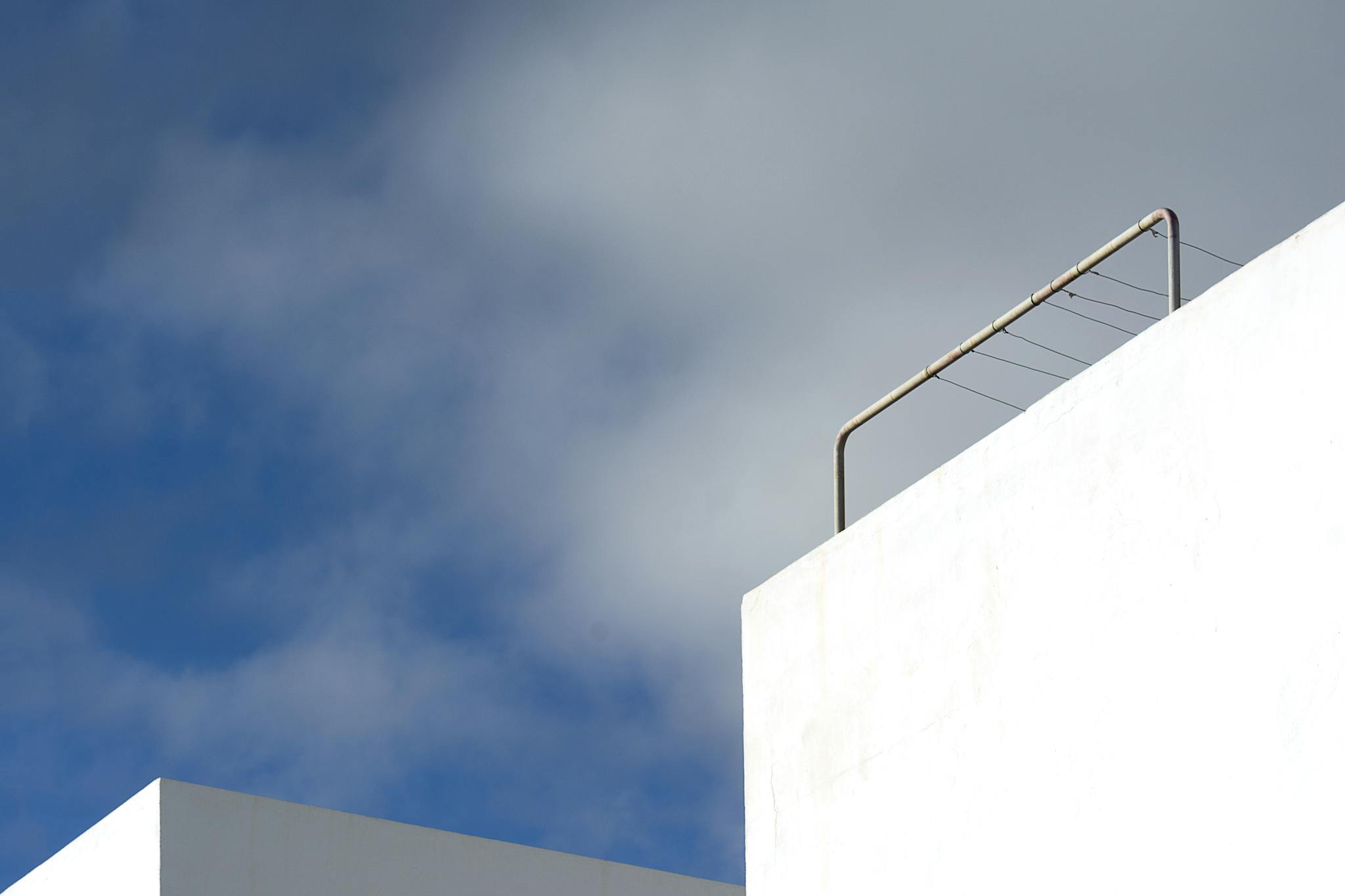 A minimalist view of white architecture with a railing against a bright cloudy sky.